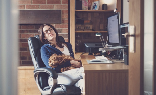 A woman is relaxing in her home office while holding a puppy